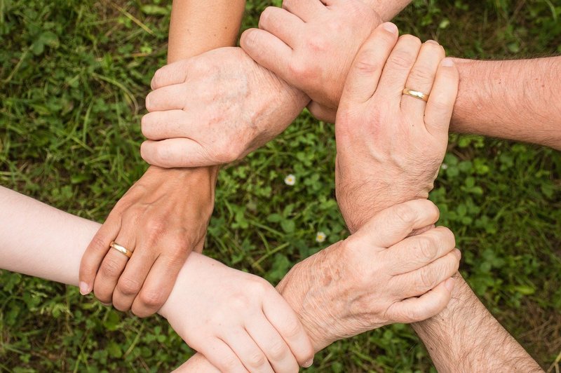 Mehrere Hände fassen sich an die Arme und bilden einen Sitz
