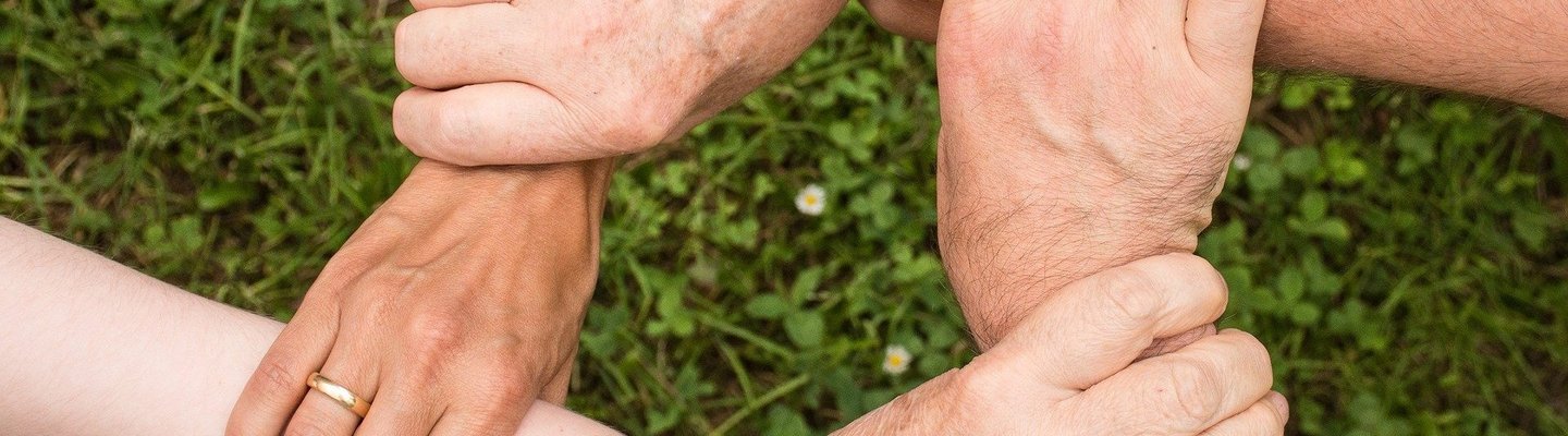 Mehrere Hände fassen sich an die Arme und bilden einen Sitz
